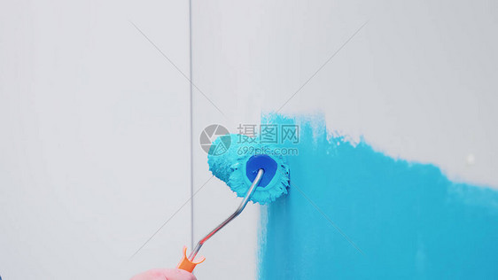 用蓝色油漆涂在墙上的滚刷在装修和改善的同时进行公寓装修和房屋建设图片
