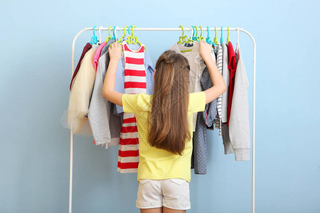 可爱开朗的小女孩选择带落地衣架的衣服图片