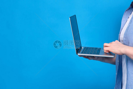 一个穿蓝衬衫的男人拿着笔记本电脑互联网上学生习材料的概念复制空图片