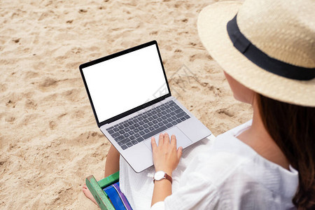 一名妇女坐在沙滩椅上时使用膝上型计算机并用空白桌面屏幕打字的妇图片