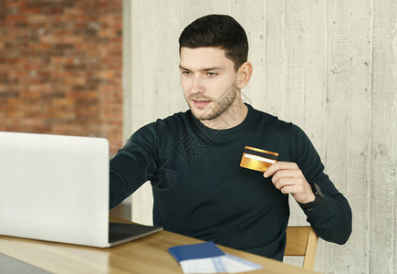 年轻人在现代办公室在线预订飞行机票和酒店坐在笔记本电脑上持有信用卡的图片