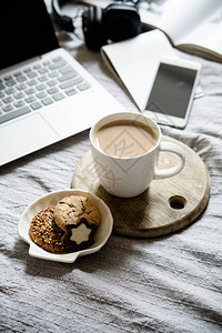 真正的家庭工作场所带咖啡的笔记本电脑床上的饼干和舒适的毯子自由职业图片