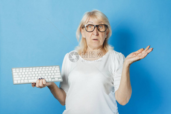 戴眼镜的老太拿着蓝色背景的键盘老年人的互联网概念新技术老年人的计算图片