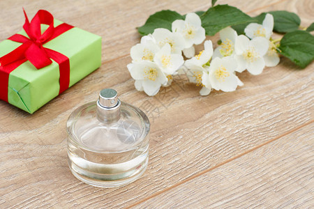 瓶装香水带有红丝带的礼品盒和木板上的茉莉花枝图片