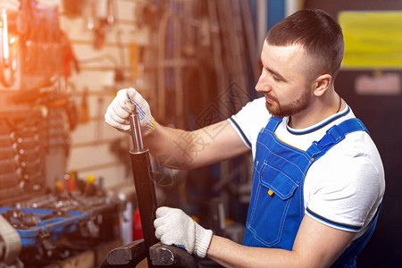 一位身穿工作服的年轻男子机械师在他的工作场所修理固定在tiches中的减震器背景图片