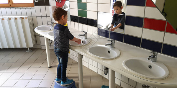 身着牛仔裤和深蓝色长袖的3岁男孩在儿童厕所房间水槽中洗手背景图片