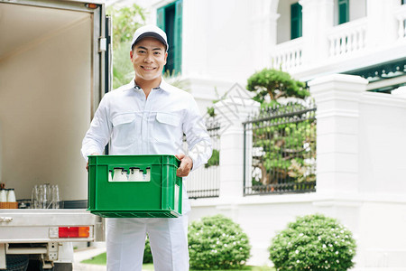 穿白色衣服站在户外用奶瓶装塑料盒和复制空间的现代牛奶工人横向中长肖像拍摄照图片