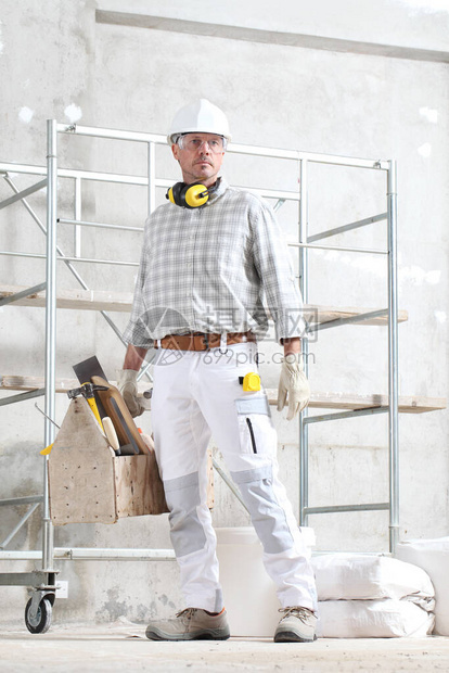 手持工具箱的男建筑工人戴手套安全帽眼镜和听力保护耳机图片