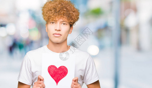 英俊的年轻帅哥拿着红心纸自信地表现在聪明的面孔图片