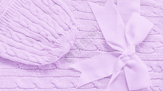 婴儿编织帽在柔软紫罗兰毯子上为新生婴儿提供可爱的弓状礼物复制空间图片