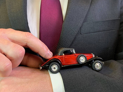 一个西装革履的男人手里拿着一辆玩具车一位商人指着一辆新车理念图片