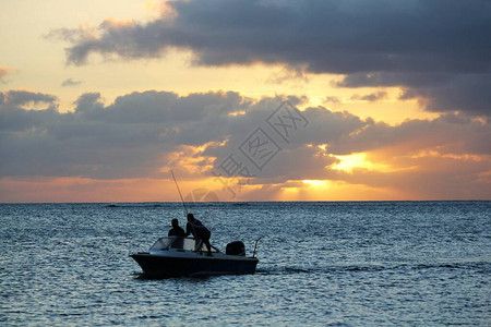 渔民在日落时分航行的船上的剪影图片