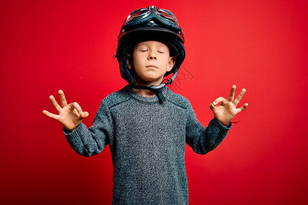 年轻的白人小孩戴着老式摩托车头盔和谷歌在红色背景上放松背景图片