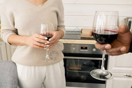 两名无法辨认的男女站在厨房里拿着红葡萄酒杯子的图片
