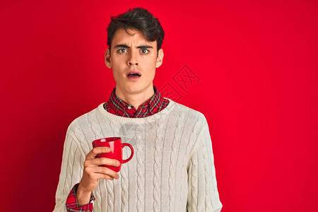 穿着冬季毛衣的少年在孤立的红色背景中喝着咖啡图片