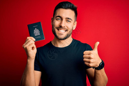 年轻英俊的游客在红色背景中持有加拿大加拿大护照图片