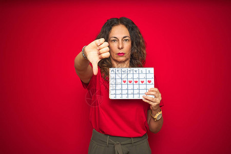 中年老妇女在红色孤立的背景下拿着月经日历图片