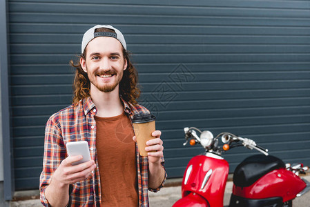年轻男子拿着纸杯咖啡和智能手机站在红图片