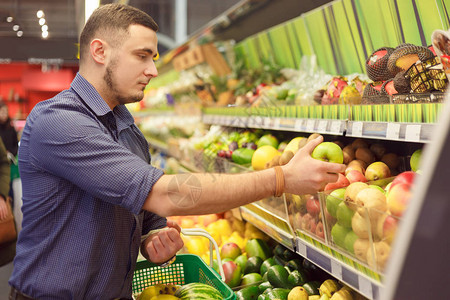 男人在超市的货架上为杂货店买水果图片