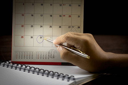 用笔在日历上写字以备笔记或制作和计划手握笔并指向图片