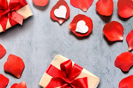 在牛皮纸上的礼物与灰色桌子上的红玫瑰花瓣背景上的心形装饰图片