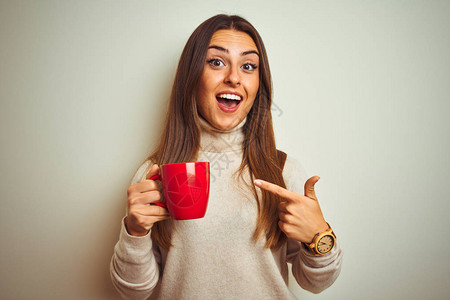 年轻漂亮的女人站在孤立的白色背景上喝着红杯咖啡图片