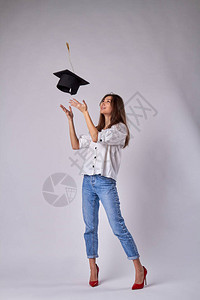 微笑的高加索女孩正在扔她的毕业帽美丽的女孩穿着牛仔裤和孤立的白色背图片