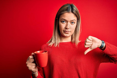 年轻美女喝着咖啡站在孤立的红色背景上图片