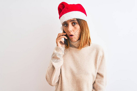 戴着圣诞帽的漂亮红发女人在智能手机上说话时惊讶地吓得脸色惊恐图片