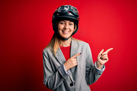 赛车手,身戴摩托车头盔的年轻金发美女骑摩托车女郎在红色背景下微笑
