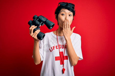 年轻美丽的亚洲救生员女孩在红色背景上用哨子和双筒望远镜捂住嘴图片