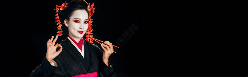 身着黑色和服头发上插着红花拿着筷子在黑色全景照片上显示出好的标志图片