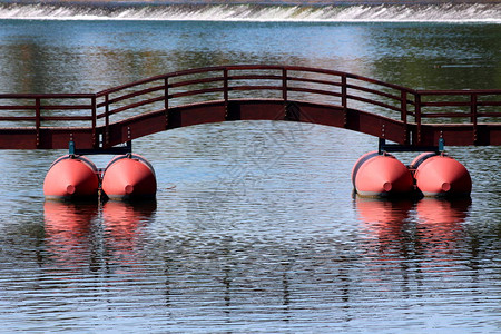 带红色浮标和中拱门的木质栅栏固定在平静的蓝河上图片