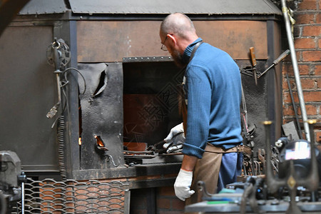 铁匠在炉子里加热铁年轻的传统铁匠用明火工作铁匠在铁匠铺里用火花烟在车间里锻造背景图片