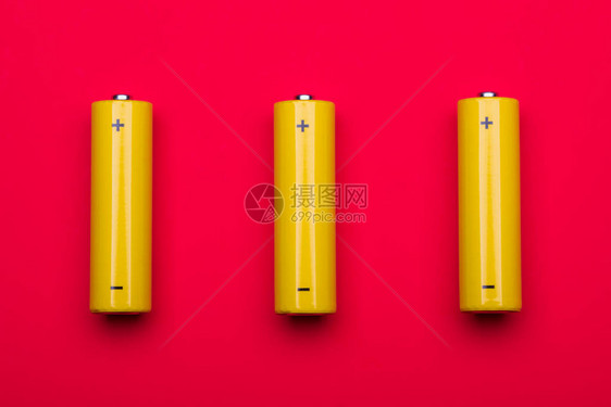 红色背景的3个黄色AA碱电池或可再充电的NiMH电池图片