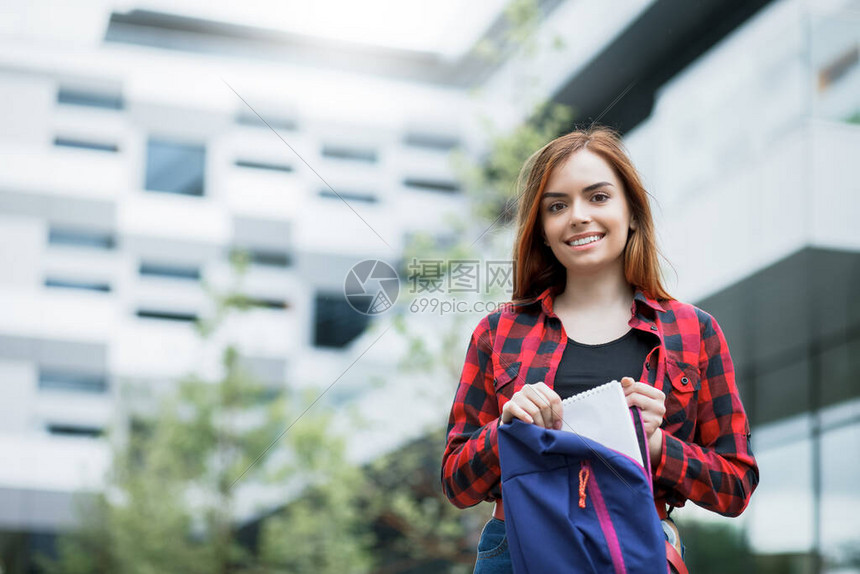女学生从背包里拿了笔记本一个校园建筑背景上可图片