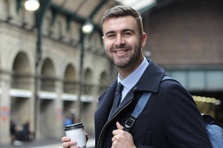 英俊的年轻商人穿着温暖大衣在火车站用纸杯图片