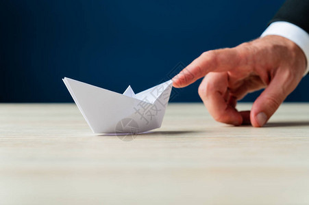 一个商人的手指向前推纸造成折纸船图片