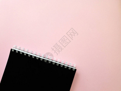 带有螺旋夹和浅粉红背景的空白黑布纸笔记纸上的顶部视图商业或教育概念图片
