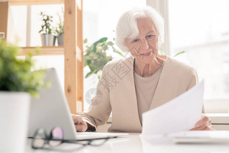 年老女经济学家或银行家在办公室膝上型电脑前坐在办公桌前图片