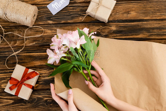 妇女将粉红花放在纸黄麻绳和木质表面的礼品盒上图片