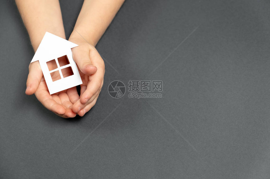 儿童手持灰色背景的白纸屋家庭住宅和房地产概念图片