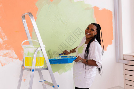 年轻快乐的非洲裔美国女人在新房子里用油漆滚筒画内墙一个女人用滚图片