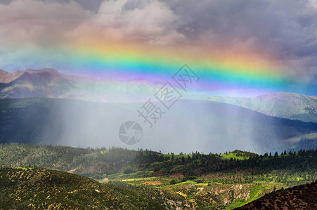 暴风雨阳光和直线彩虹笼罩在山上的一片绿山谷上背景图片