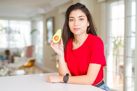 年轻女人吃健康的鳄梨自信地表现在聪明的面孔图片