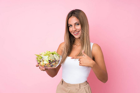 年轻的金发女人在孤立的背景下吃沙拉图片