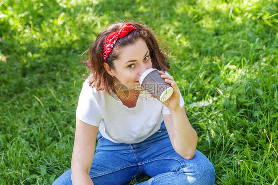 快乐的女孩微笑着在户外吃午饭美丽的年轻黑发女人带走基于公园或花园绿草背景的咖啡杯教育自由职业者图片