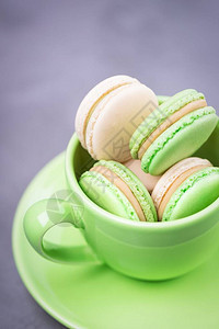 自制法式马卡龙或马卡龙带饼干的绿色杯子灰色背景上带有香草奶油的薄荷饼图片