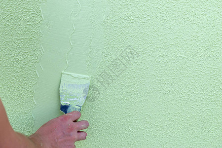 工匠手不带一根手指握着石膏和涂在绿色混凝土上的石膏的弹片图片