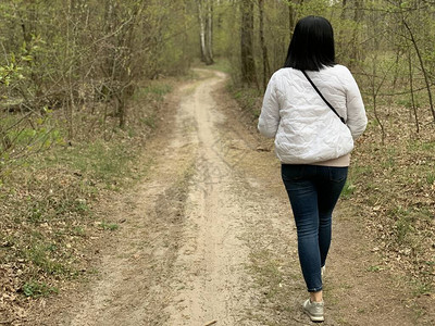 穿着夹克和牛仔裤的女人正在森林中走着一条路图片